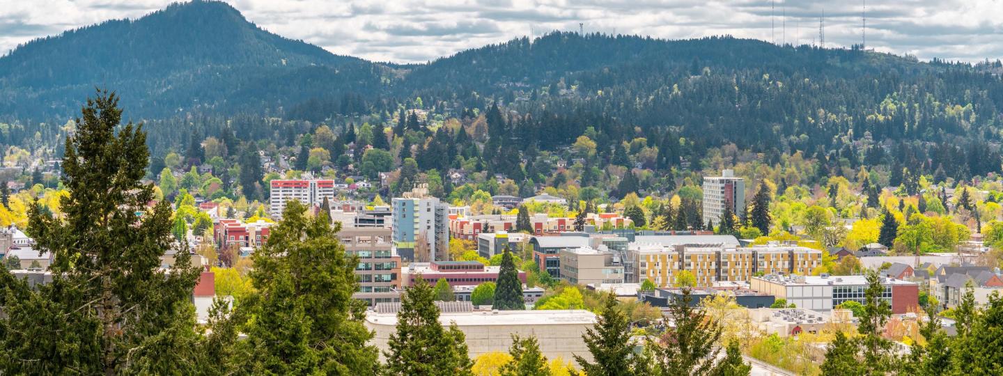 Buildings of downtown Eugene framed by trees in the foreground and Spencer Butte in the background.