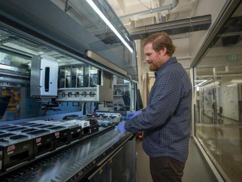 A person stands in front of a liquid handling platform in the G C 3 F core facility.