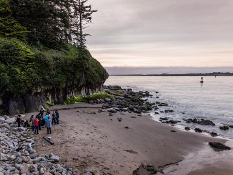 A small group of people stand on a rocky ocean beach.